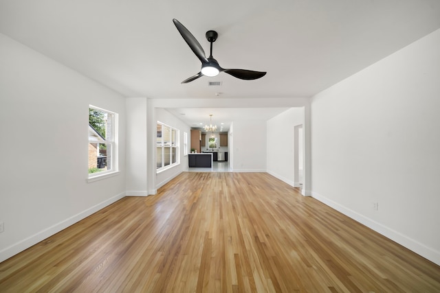 unfurnished living room with a chandelier, light wood-style flooring, a ceiling fan, and baseboards