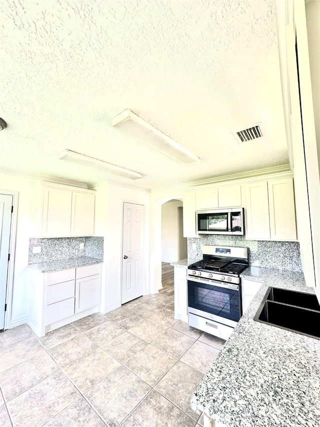 5006 Dawngate Dr, Spring, TX 77373 - kitchen featuring stainless steel appliances, arched walkways, tasteful backsplash, white cabinetry, and a textured ceiling