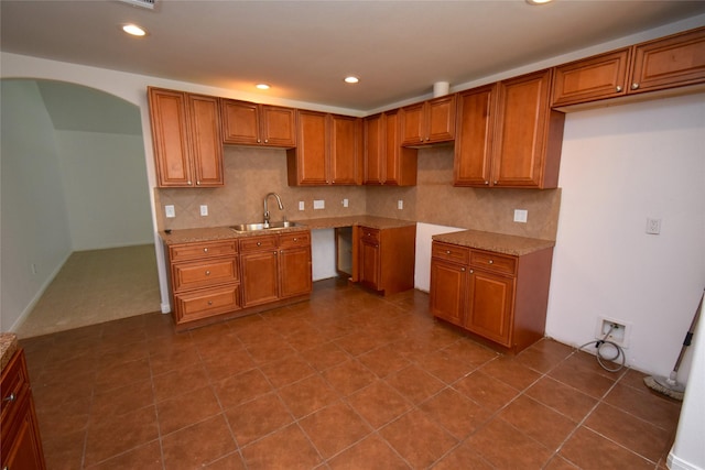 kitchen with a sink, arched walkways, brown cabinetry, and recessed lighting