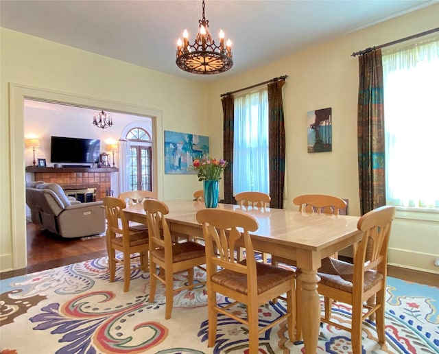 dining space with a chandelier, wood finished floors, a tiled fireplace, and baseboards