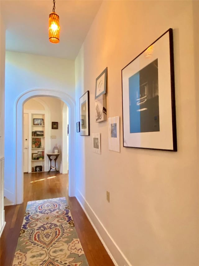 hallway featuring arched walkways, dark wood-type flooring, and baseboards