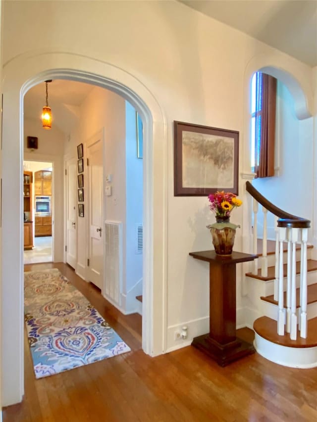 hallway with arched walkways, wood finished floors, baseboards, and stairs