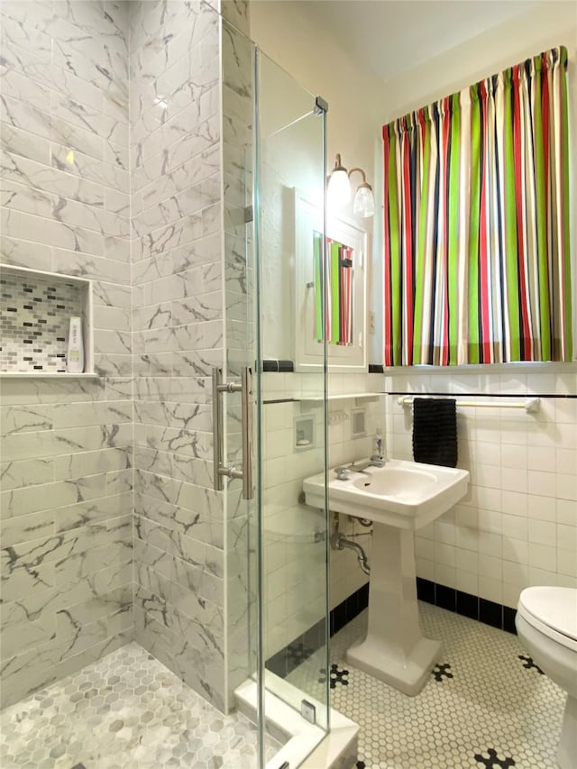 bathroom with a shower stall, tile walls, tile patterned floors, toilet, and wainscoting