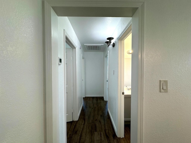 hallway with dark wood-style floors, attic access, baseboards, and a textured wall
