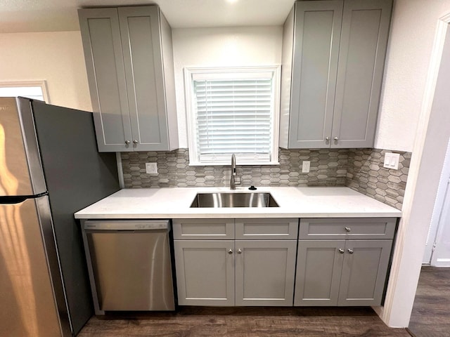 kitchen with gray cabinetry, stainless steel appliances, a sink, and backsplash