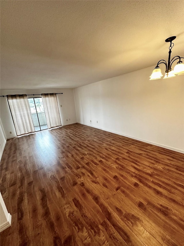 unfurnished room with dark wood finished floors, a chandelier, a textured ceiling, and baseboards