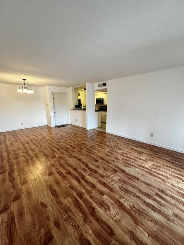 unfurnished living room featuring dark wood-style floors, a chandelier, and baseboards