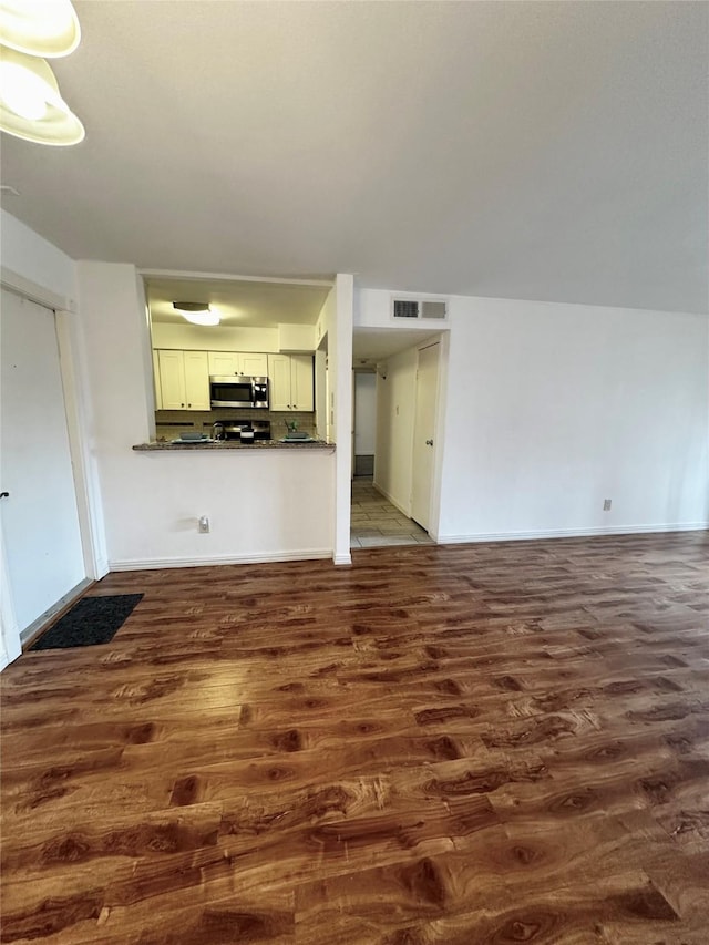 unfurnished living room featuring dark wood-type flooring and baseboards