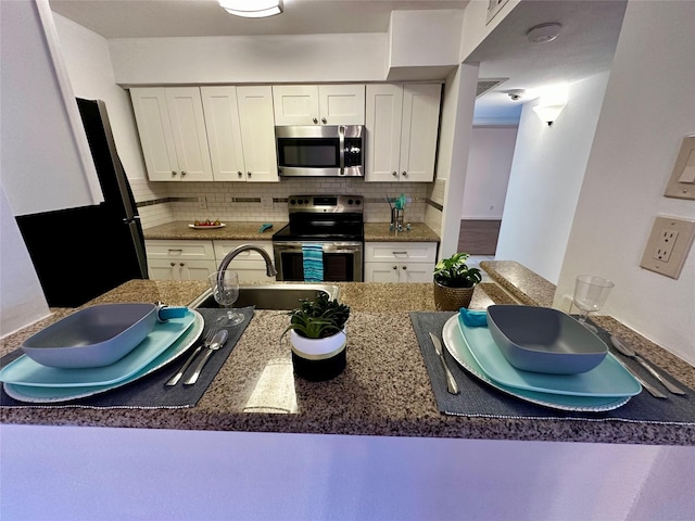 kitchen with stainless steel appliances, a sink, backsplash, white cabinets, and dark stone countertops