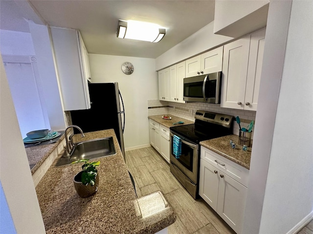 kitchen with stainless steel appliances, a sink, backsplash, light wood-style floors, and white cabinetry