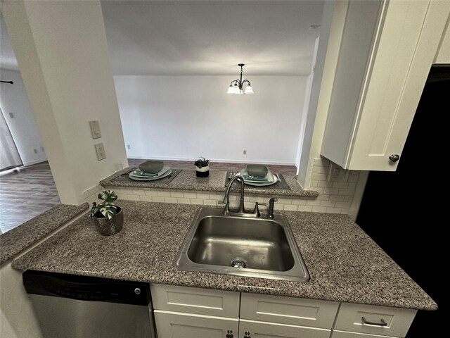kitchen featuring a sink, dishwasher, white cabinetry, decorative backsplash, and a chandelier