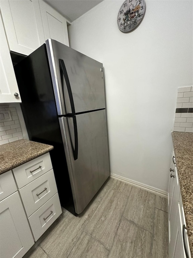 kitchen with freestanding refrigerator, decorative backsplash, white cabinets, light wood-style flooring, and stone counters