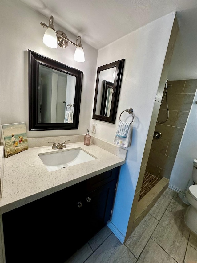 full bathroom with toilet, a tile shower, vanity, and tile patterned floors