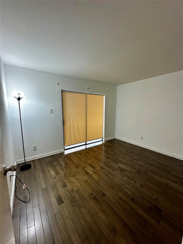 unfurnished room with dark wood-style flooring, a textured ceiling, and baseboards