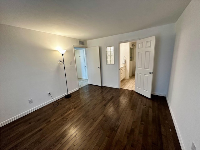 unfurnished bedroom with wood-type flooring, baseboards, and connected bathroom