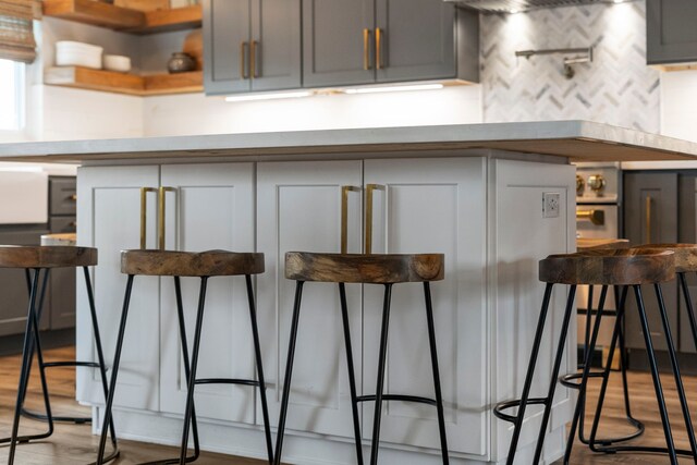 30 N Curlew St, La Marque, TX 77568 - kitchen with light wood-style floors, backsplash, gray cabinetry, a breakfast bar area, and open shelves
