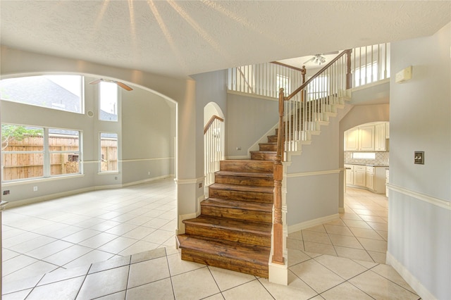 6613 Whitton Dr, Houston, TX 77085 - stairs featuring tile patterned flooring, a ceiling fan, a textured ceiling, arched walkways, and baseboards