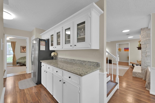 kitchen with dark wood-style floors, a textured ceiling, white cabinets, glass insert cabinets, and light stone counters
