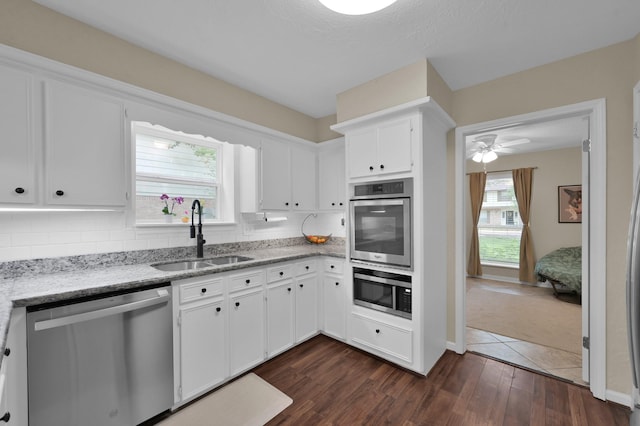 kitchen featuring stainless steel appliances, a sink, backsplash, dark wood finished floors, and light stone counters