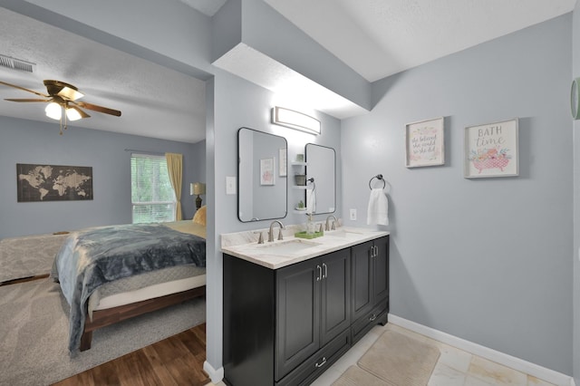 ensuite bathroom with baseboards, double vanity, a ceiling fan, and a textured ceiling
