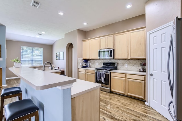 18115 Linden Forest Ln, Katy, TX 77449 - kitchen featuring stainless steel appliances, light brown cabinetry, arched walkways, backsplash, and a sink