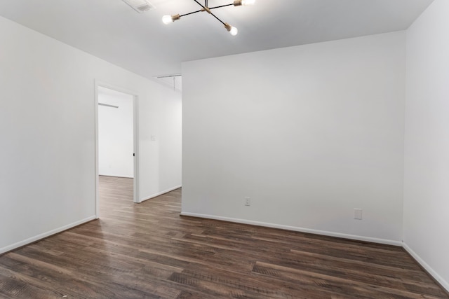 spare room featuring a chandelier, dark wood-type flooring, baseboards, and attic access