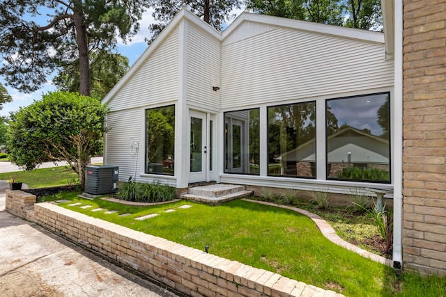rear view of property with central air condition unit and a lawn