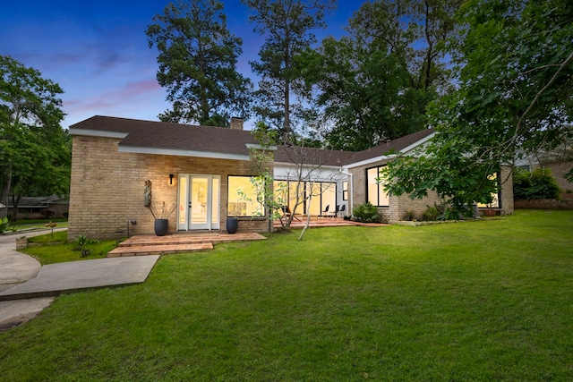 back of house at dusk featuring a chimney, brick siding, and a lawn
