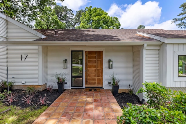 doorway to property featuring roof with shingles, board and batten siding, and a patio