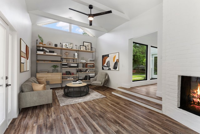 living area with high vaulted ceiling, wood finished floors, a brick fireplace, and ceiling fan