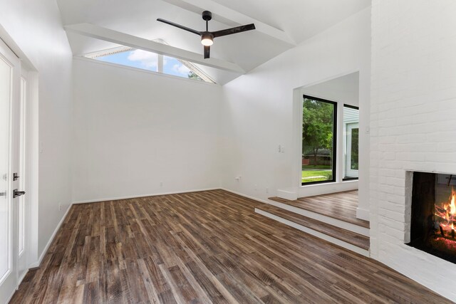 unfurnished living room with high vaulted ceiling, a brick fireplace, wood finished floors, ceiling fan, and baseboards