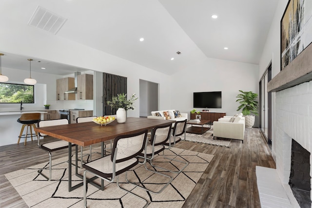 dining space with wood finished floors, a brick fireplace, high vaulted ceiling, and recessed lighting