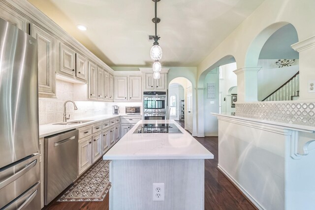 147 Sunnyvale W, Montgomery, TX 77356 - kitchen featuring appliances with stainless steel finishes, a sink, a kitchen island, arched walkways, and backsplash