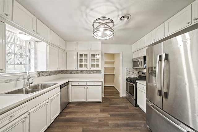 kitchen featuring appliances with stainless steel finishes, backsplash, a sink, white cabinetry, and dark wood-style flooring