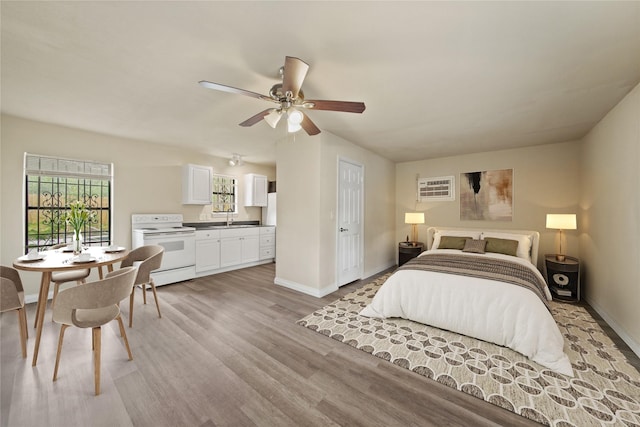 bedroom featuring a sink, baseboards, light wood-type flooring, ensuite bath, and a wall mounted AC
