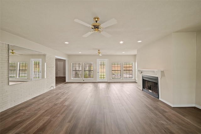 unfurnished living room featuring ceiling fan, a fireplace, wood finished floors, brick wall, and baseboards