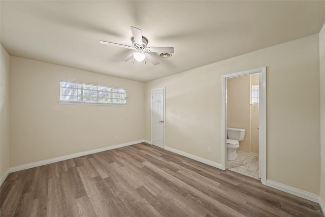 unfurnished bedroom featuring wood finished floors, ensuite bath, baseboards, and a ceiling fan