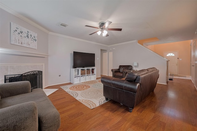 living room featuring a ceiling fan, wood finished floors, baseboards, crown molding, and stairway