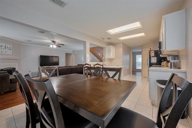 dining space with light tile patterned floors, a ceiling fan, a skylight, and crown molding