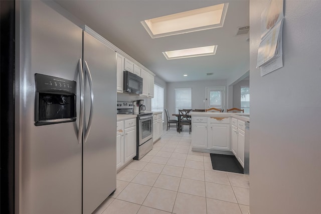 kitchen with stainless steel appliances, light tile patterned floors, white cabinets, and healthy amount of natural light