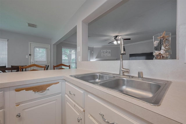 kitchen with a sink, light countertops, white cabinets, a ceiling fan, and crown molding