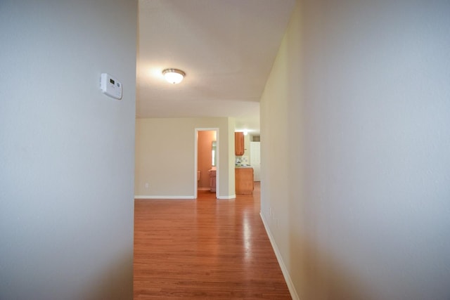 hallway featuring light wood finished floors and baseboards