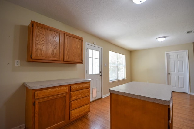 kitchen featuring light wood-type flooring, brown cabinetry, a kitchen island, a textured ceiling, and light countertops
