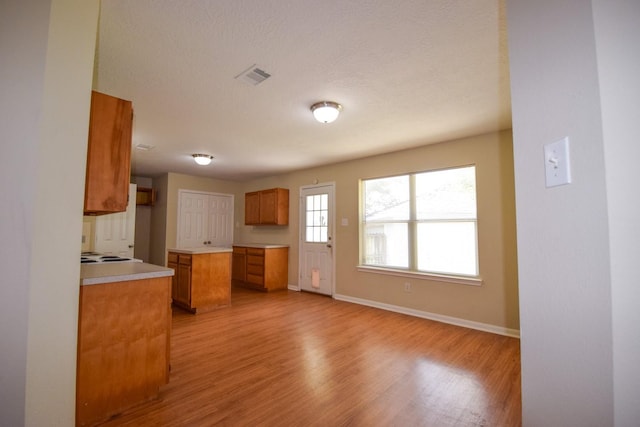 kitchen with brown cabinetry, light wood-style flooring, baseboards, light countertops, and a textured ceiling
