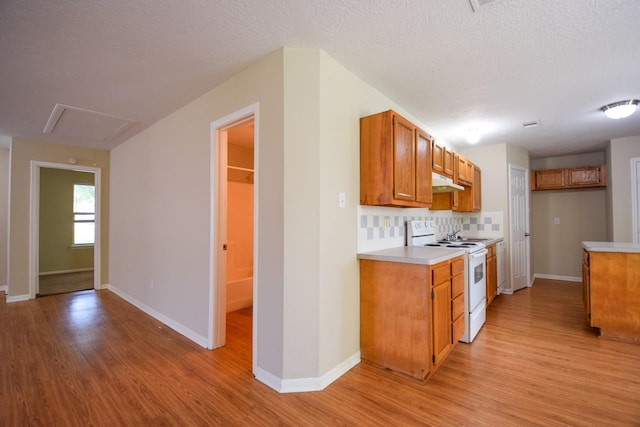kitchen with white electric stove, under cabinet range hood, light wood-style floors, light countertops, and brown cabinetry