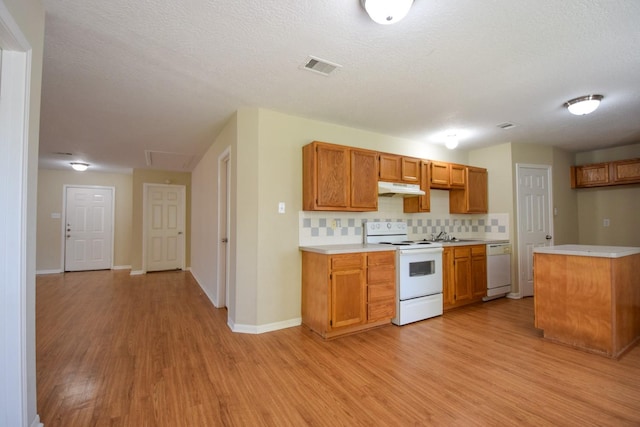 kitchen featuring white appliances, under cabinet range hood, light wood-type flooring, light countertops, and a textured ceiling