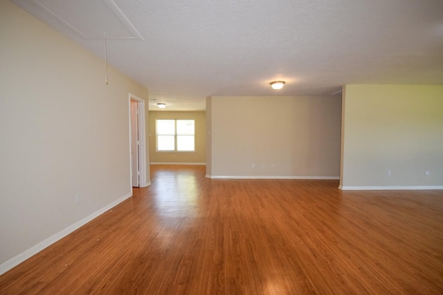 spare room featuring attic access, baseboards, and wood finished floors