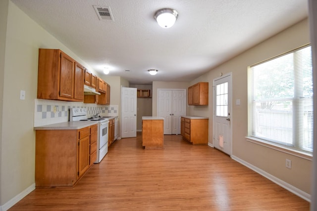 kitchen featuring electric range, light wood-style flooring, brown cabinetry, light countertops, and a textured ceiling