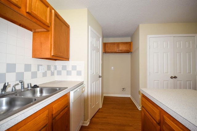 kitchen featuring white dishwasher, brown cabinets, dark wood finished floors, a sink, and light countertops