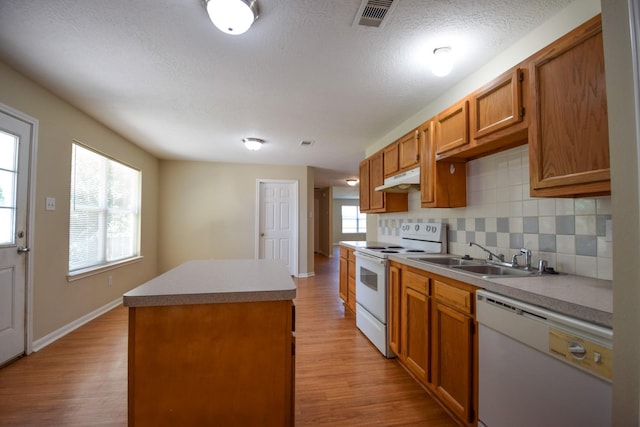 kitchen with white appliances, a sink, under cabinet range hood, a kitchen island, and light wood finished floors